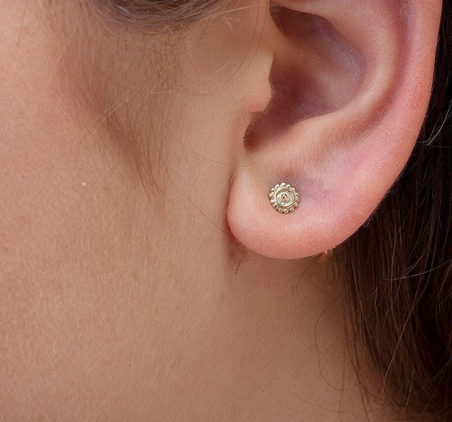 A close-up view of a person's ear with a small, gold-colored earring in the earlobe.