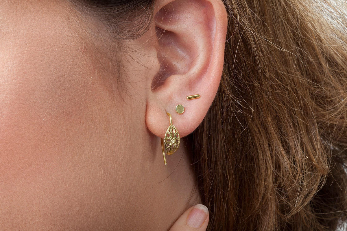 A close-up view of a person's ear adorned with a pair of gold earrings, including a dangling earring and a pair of small circular earrings.