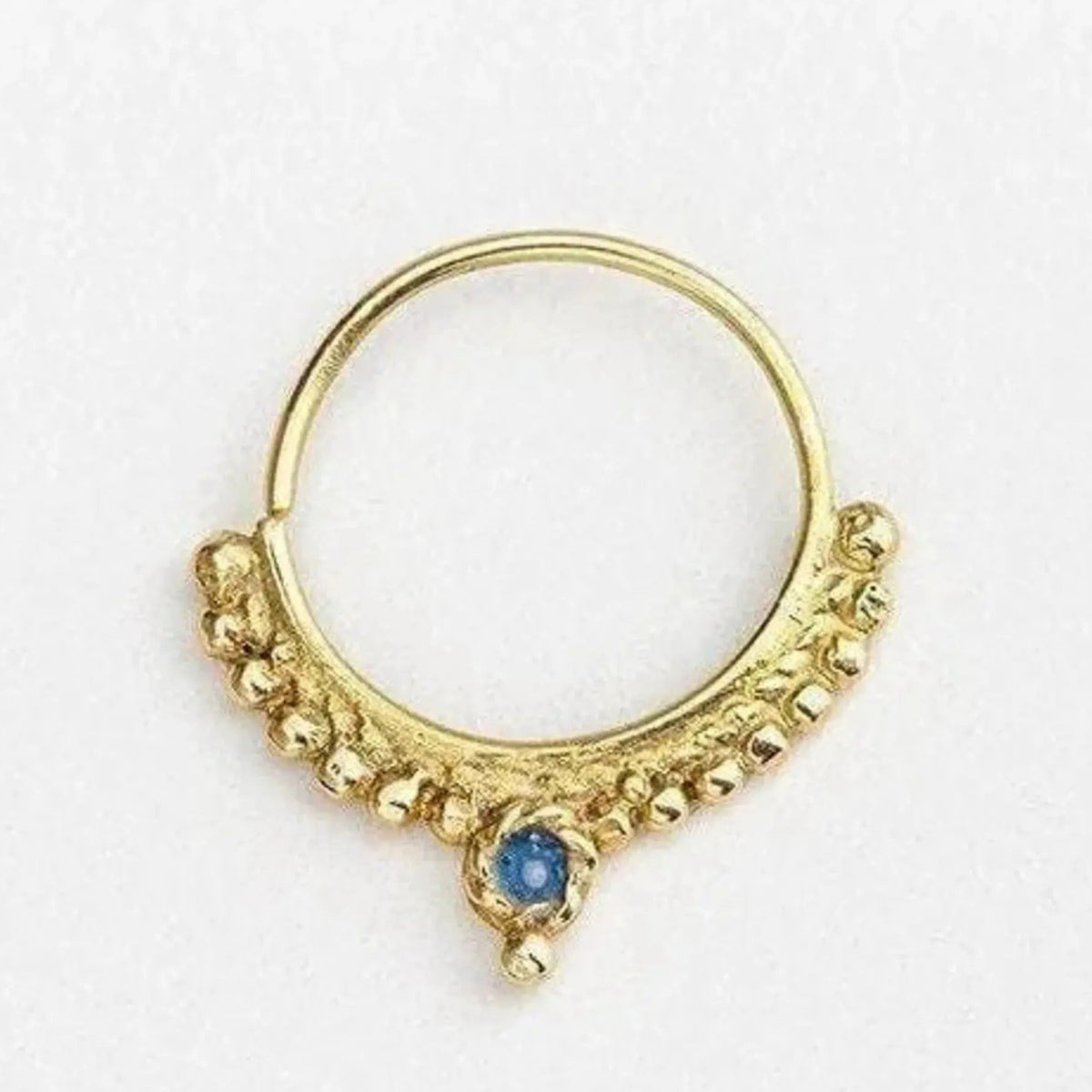 A gold-colored nose ring with a blue gemstone in the center.