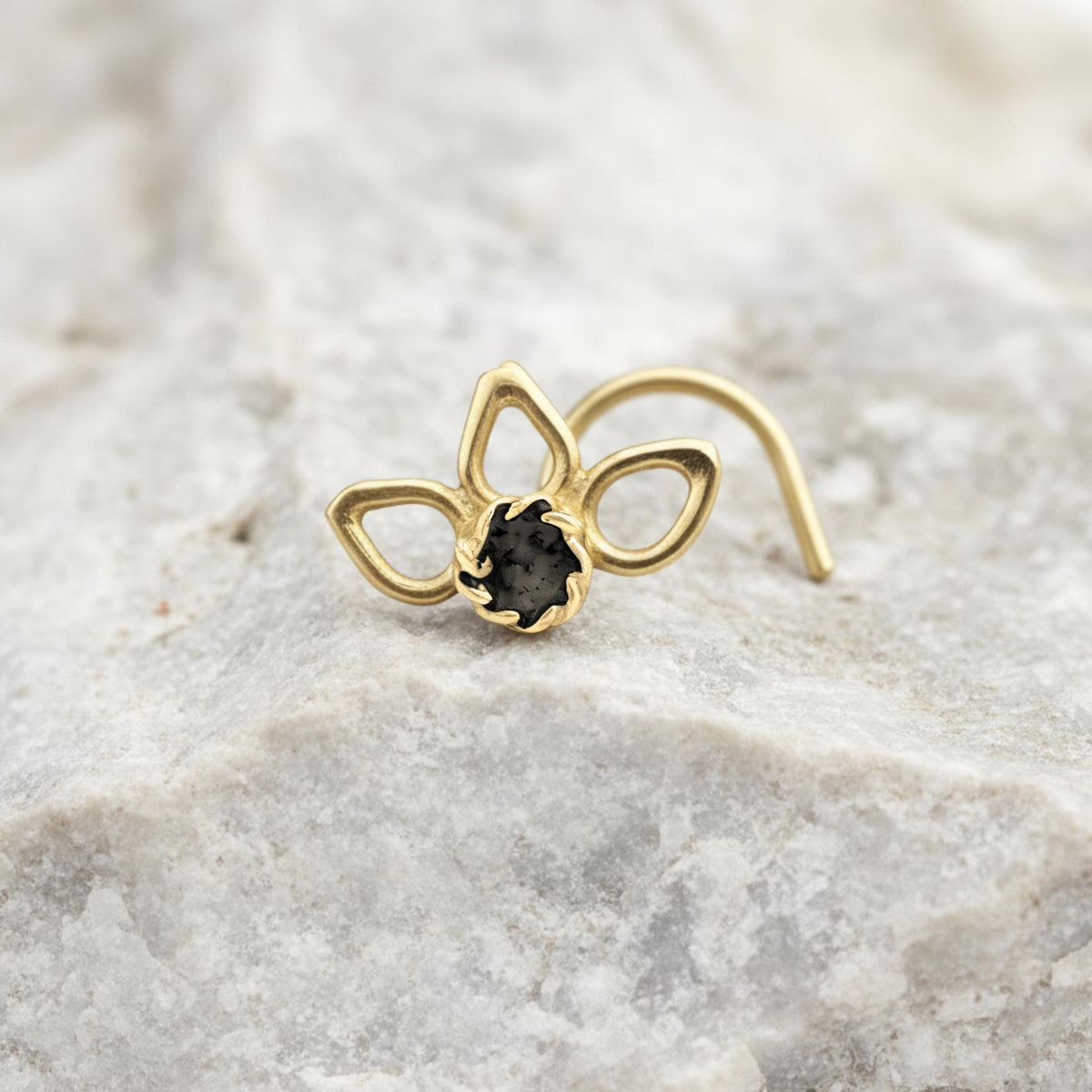 A gold-colored nose ring with a black gemstone is resting on a white marble surface.