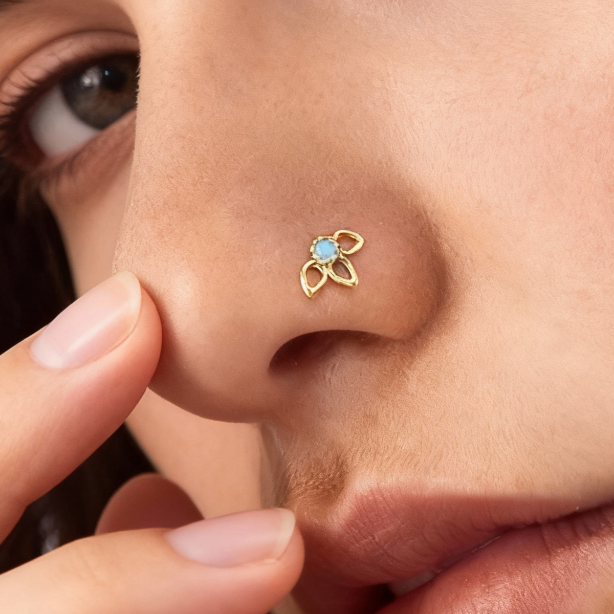 A close-up of a person's nose with a small gold nose ring featuring a blue gemstone.