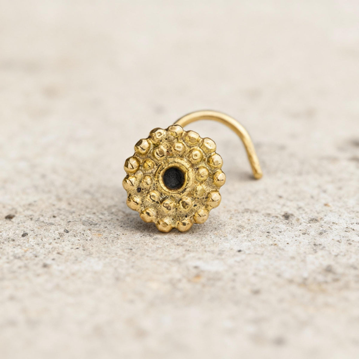 A gold-colored nose ring with a small black center is shown against a light-colored background.