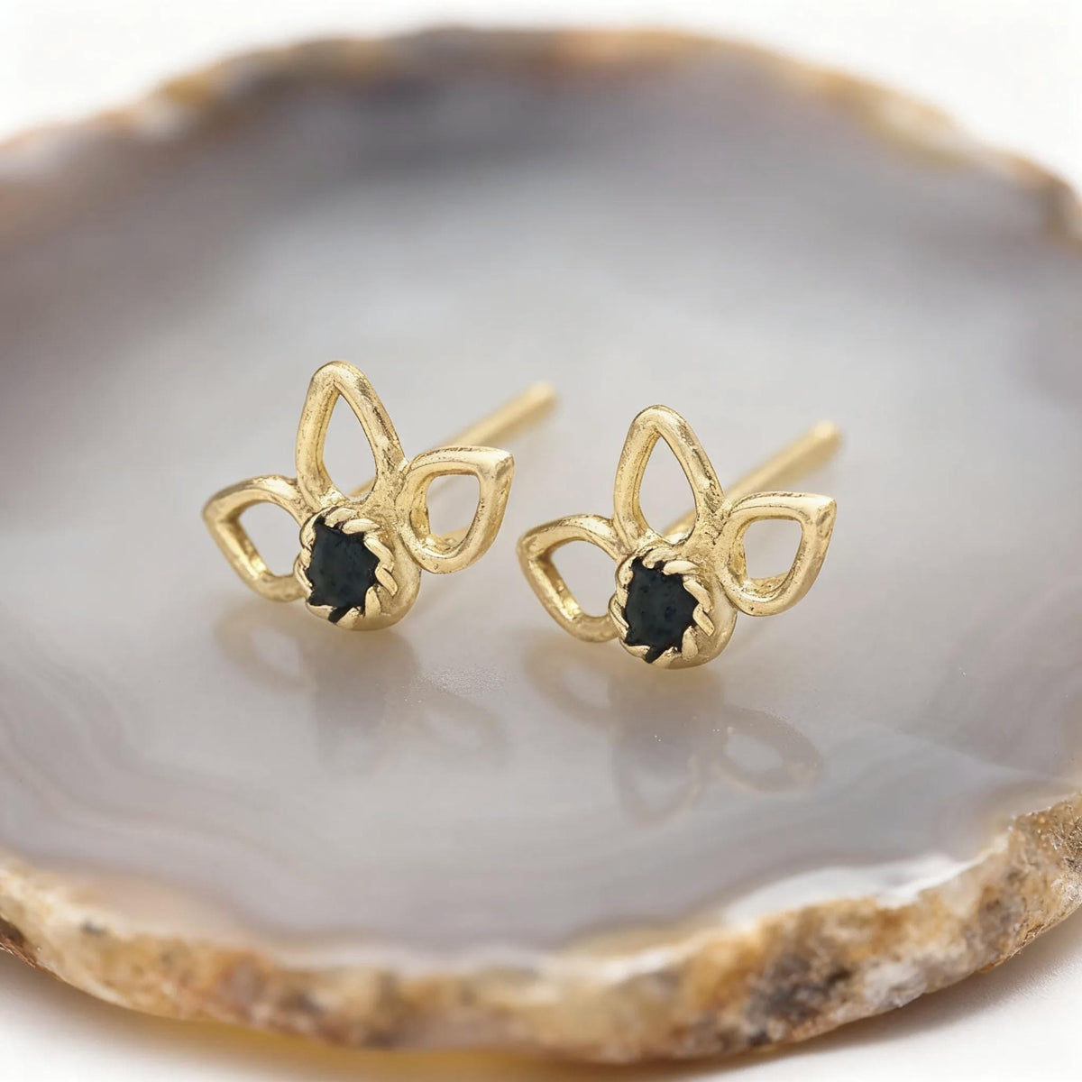 A pair of gold earrings with black gemstones, placed on a white and brown stone surface.