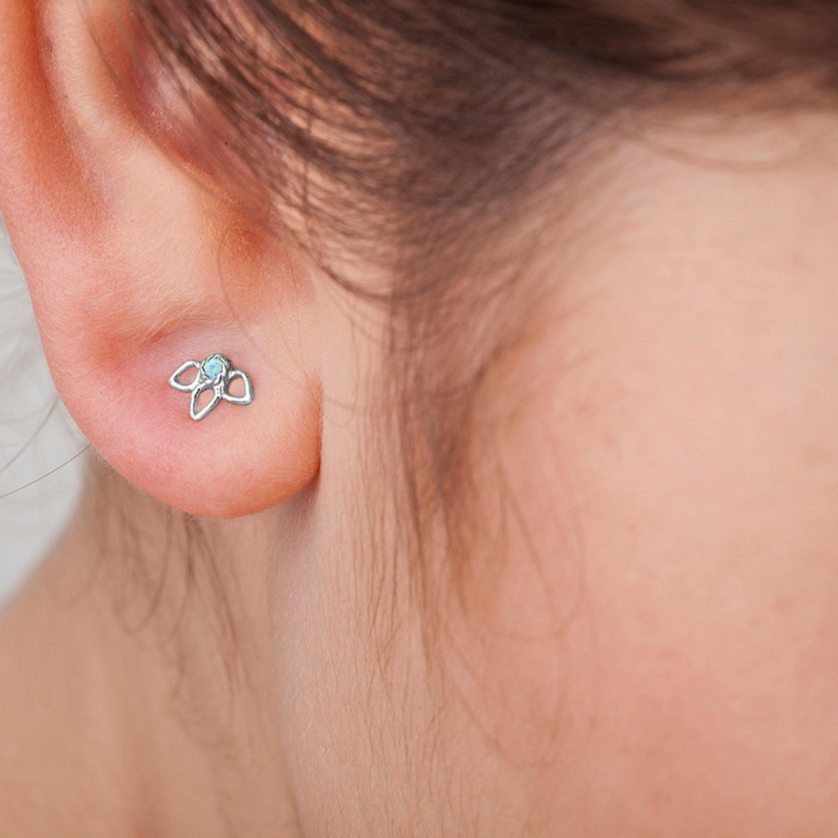 A close-up view of a person's ear with a small, silver earring featuring a floral design.