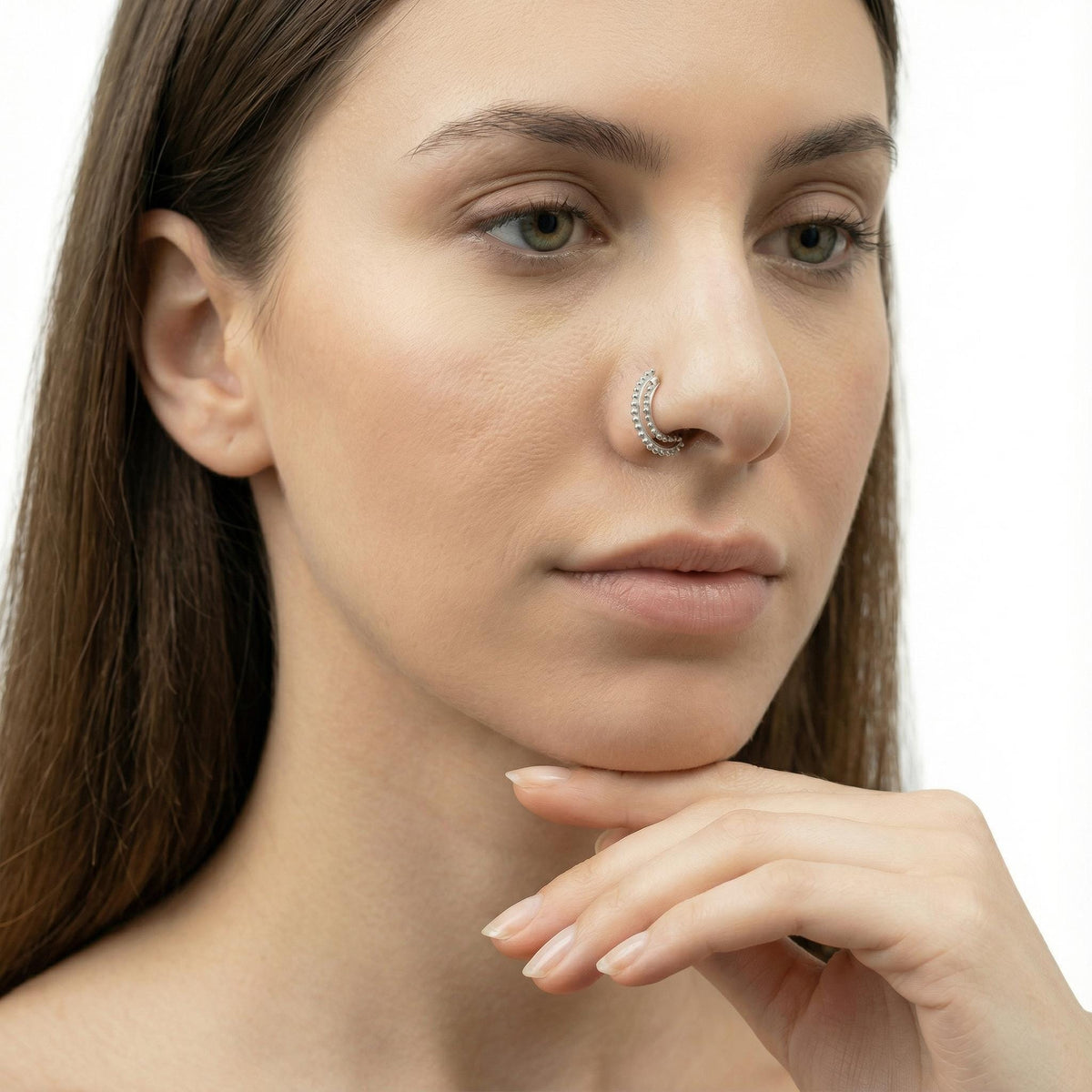 A close-up portrait of a woman with long brown hair, wearing a nose ring, and looking pensively at something off-camera.