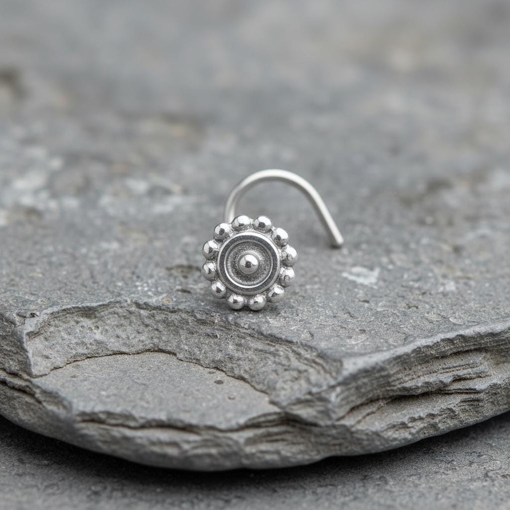 A silver nose ring with a circular design sits on a gray rock.