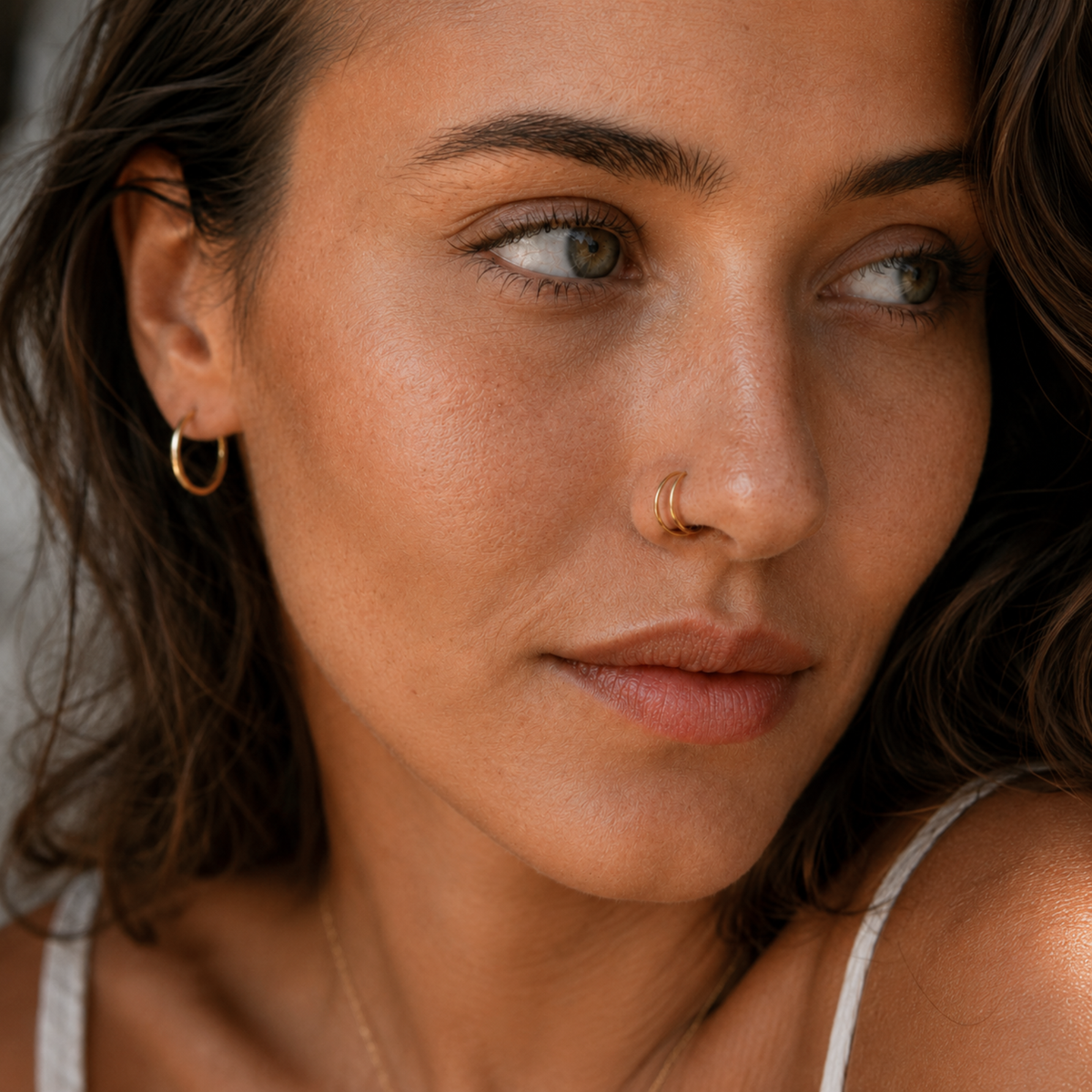 A close-up portrait of a woman with dark hair and a nose ring, looking pensively to the side.