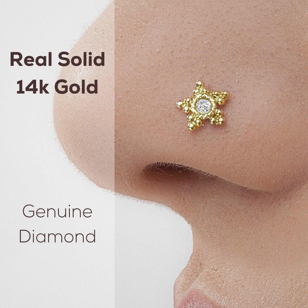 Diamond Star Nose Stud: a close-up of a person's nose with a 14k gold nose ring featuring a diamond-like gemstone.
