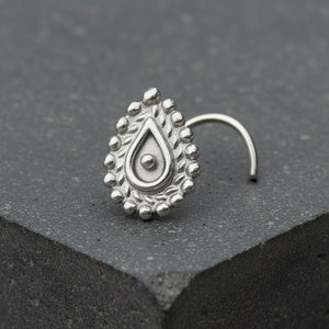 Indian Style Nose Stud: A silver nose ring with an ornate, teardrop-shaped design sits on a gray surface.