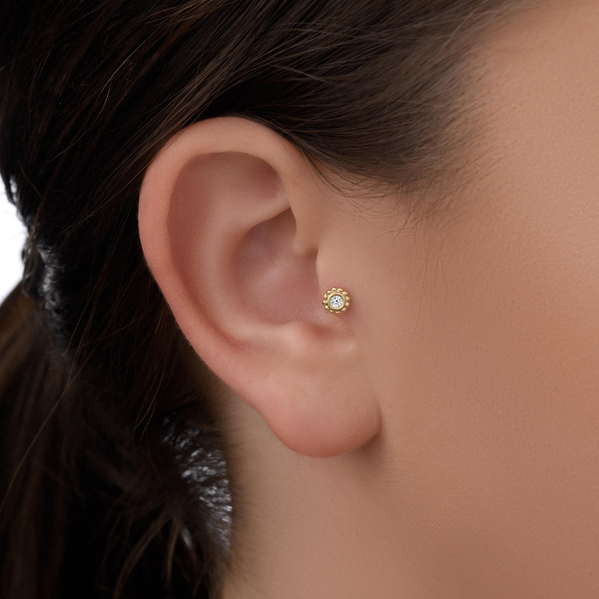 A close-up view of a person's ear with a small gold earring in the earlobe.
