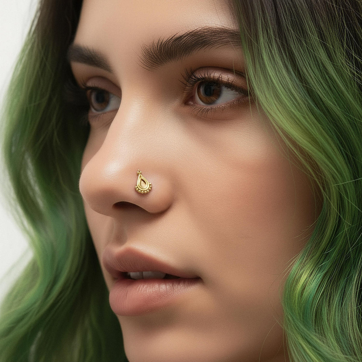 A close-up of a woman's face with green hair, wearing a gold nose ring.