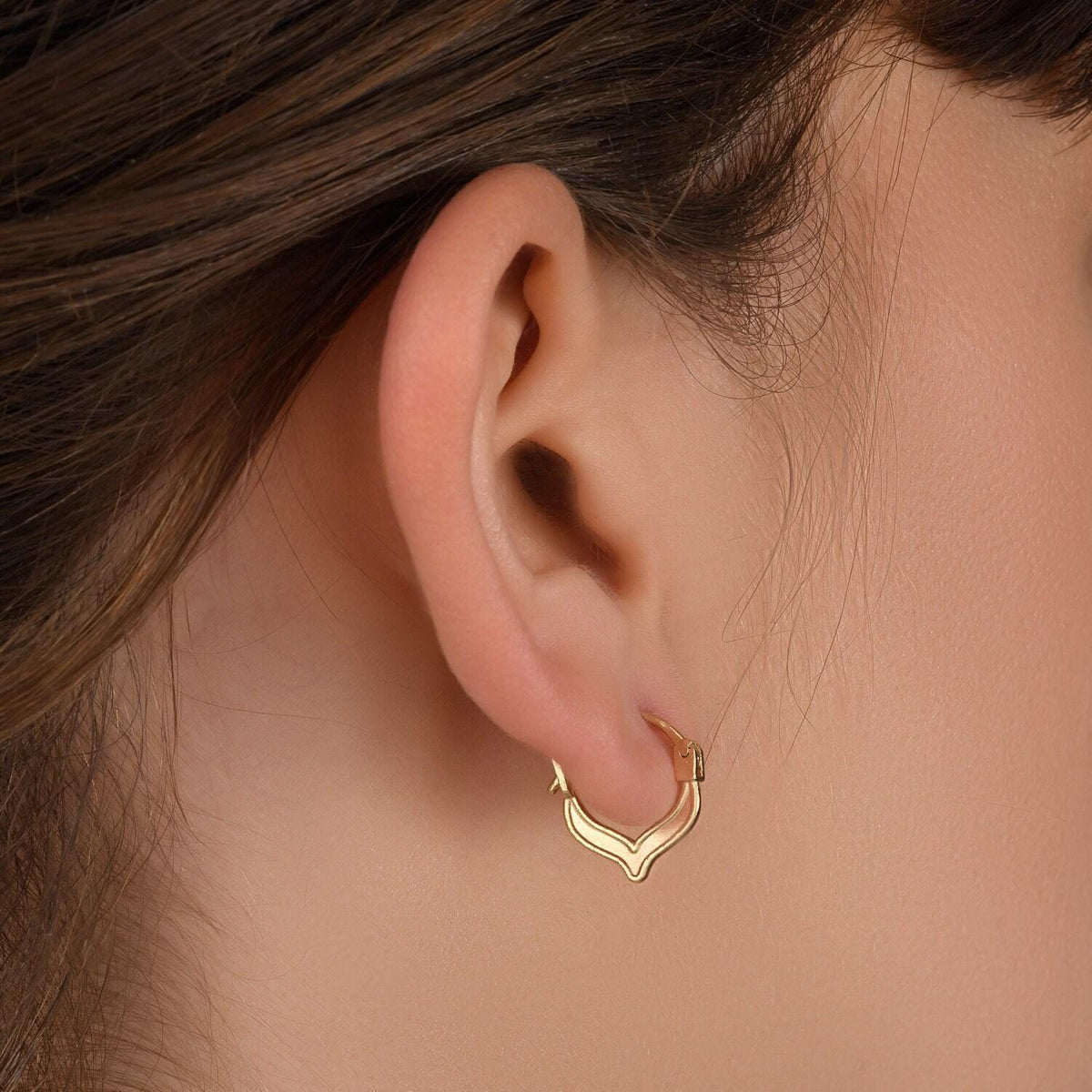 A close-up view of a person's ear adorned with a gold hoop earring.