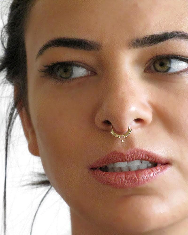 A close-up of a woman's face, focusing on her nose and lips, with a gold nose ring visible.