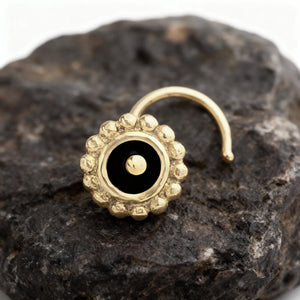 A gold-colored nose ring with a black center is resting on a dark, rocky surface.