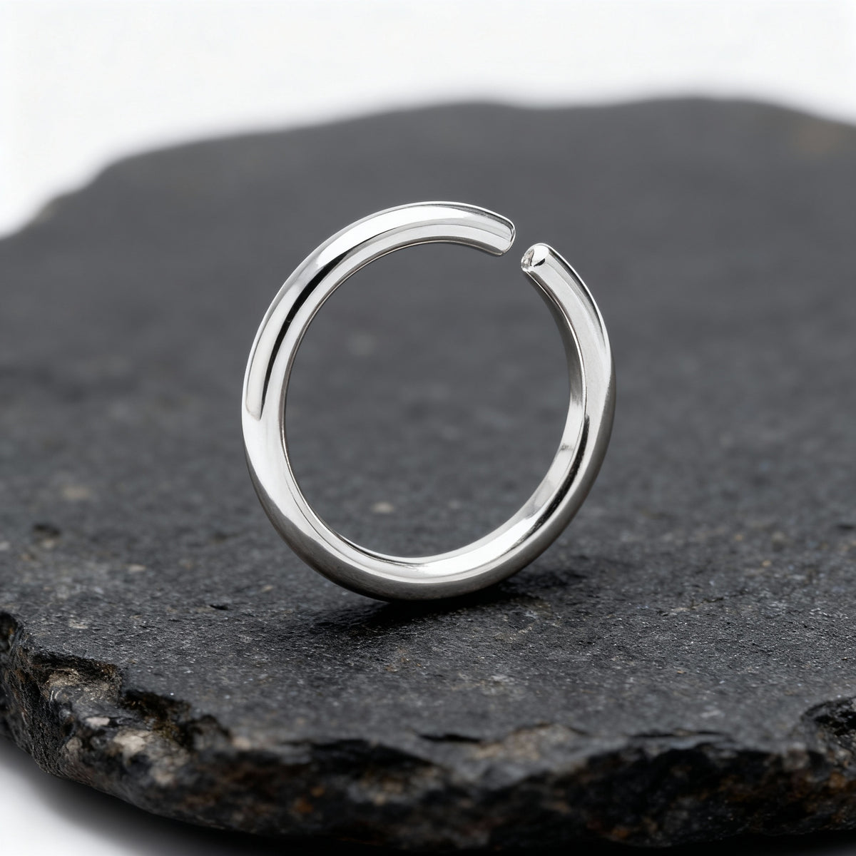 A silver ring with a unique, curved design is resting on a dark, textured surface.