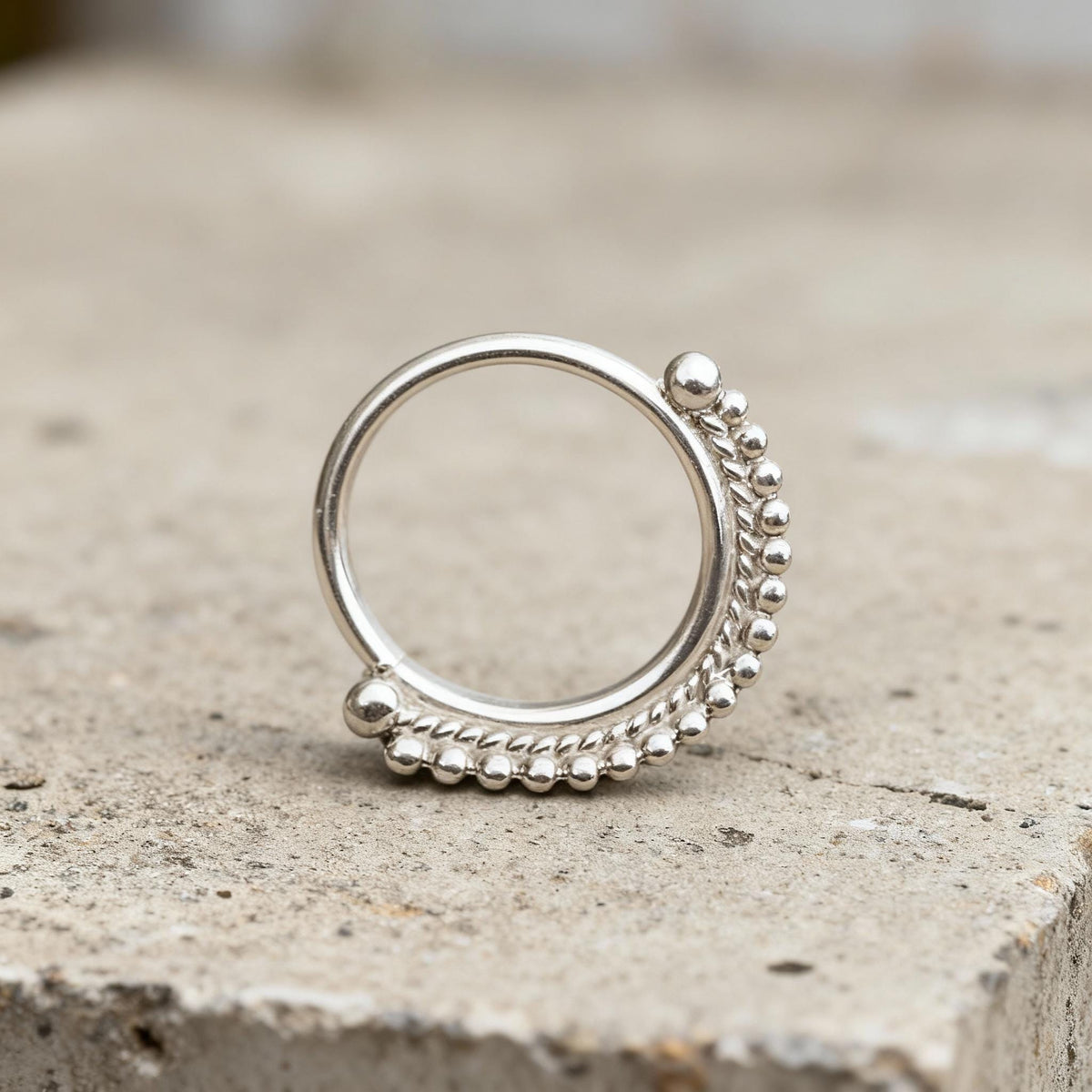 A silver ring with a decorative design on the surface it is placed on.