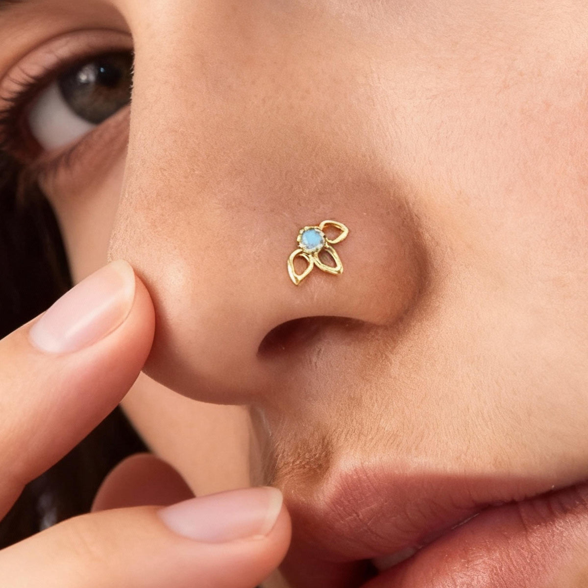 A close-up of a person's nose with a small gold nose ring featuring a blue gemstone.