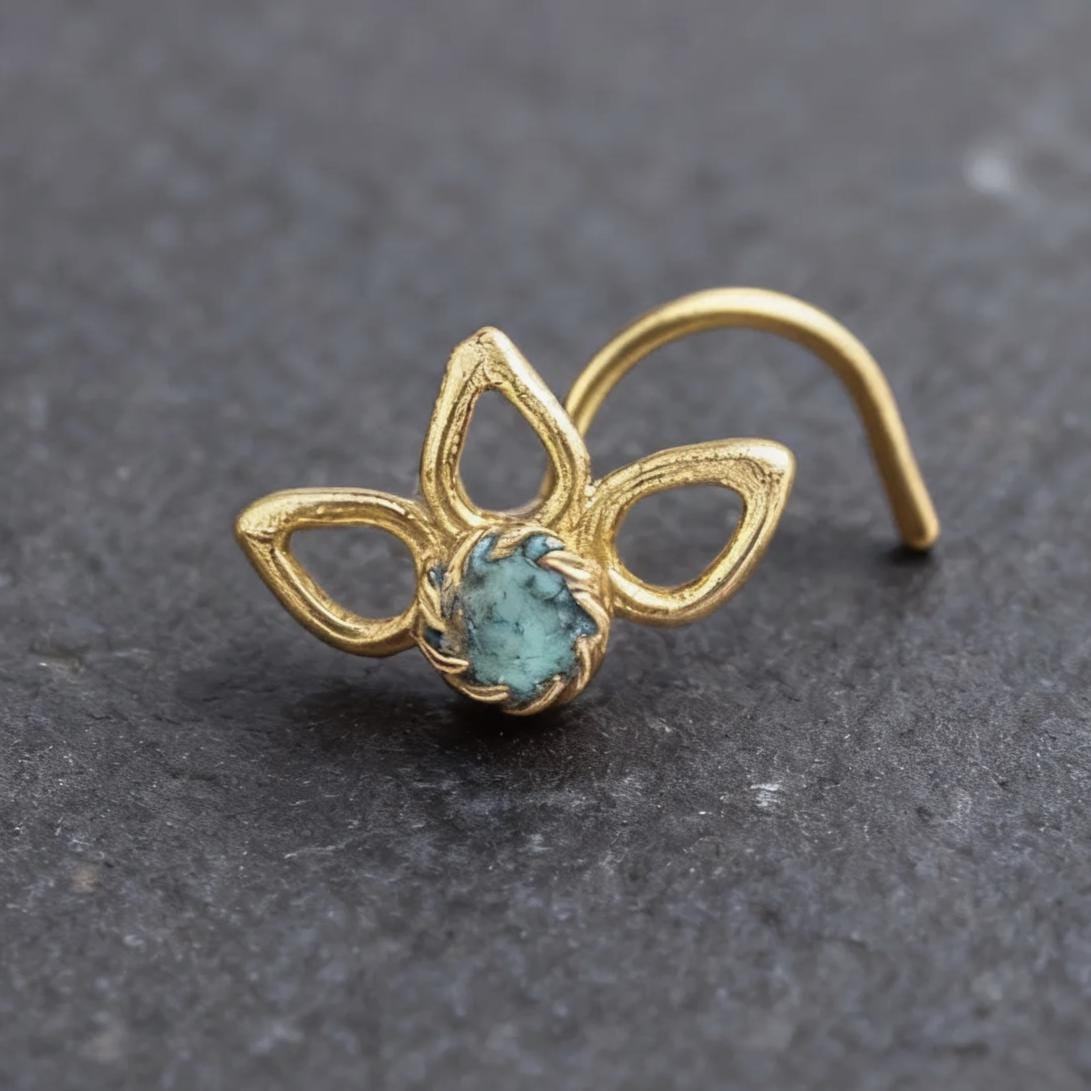 A gold-colored nose ring with a turquoise stone in the center is displayed on a dark gray surface.