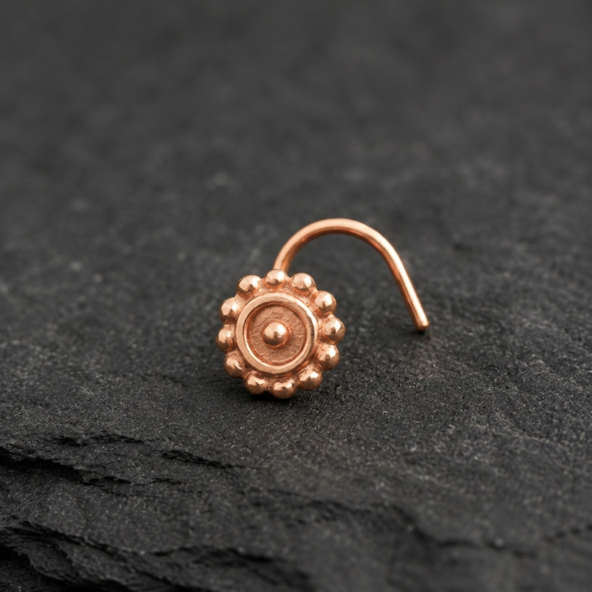A copper-colored nose ring with a circular design is resting on a dark surface.