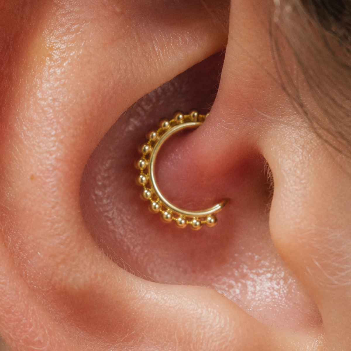 A close-up view of a person's ear with a gold-colored hoop earring in the earlobe.