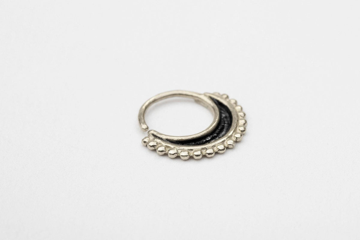 A silver-colored metal ring with a black, decorative element on the outside, resting on a plain white background.