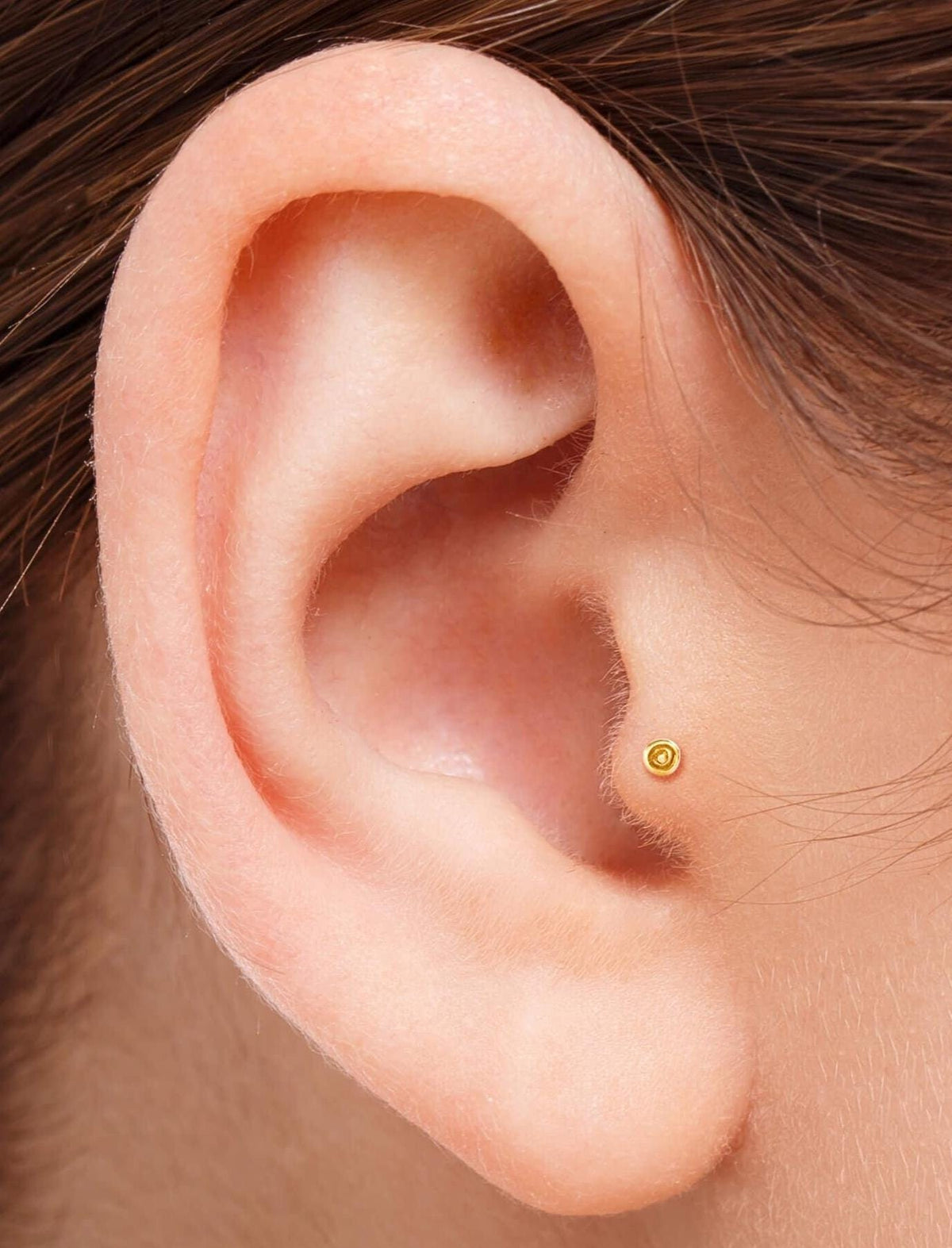 A close-up view of a person's ear, showing a small gold earring in the earlobe.