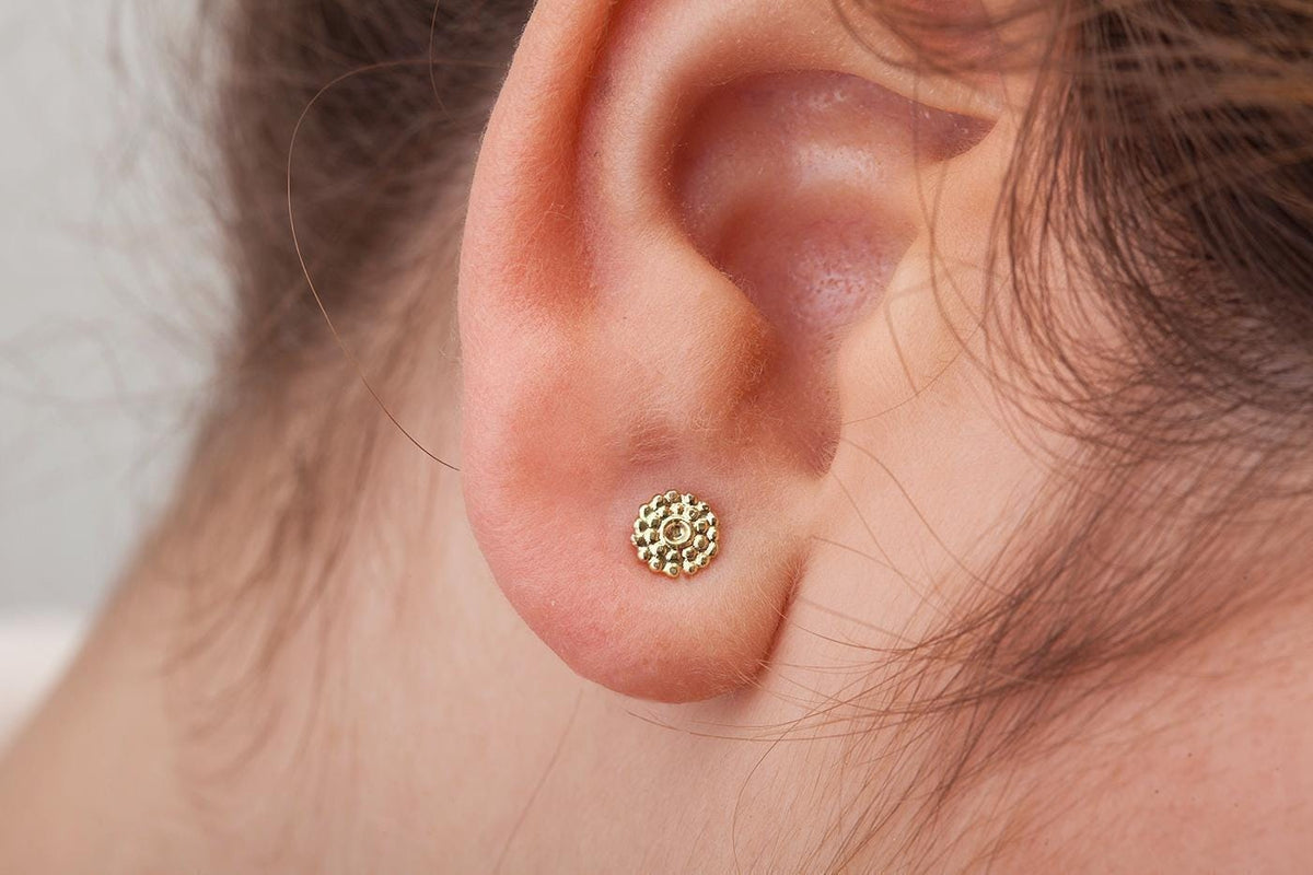 A close-up view of a person's ear with a small, round gold earring in the earlobe.