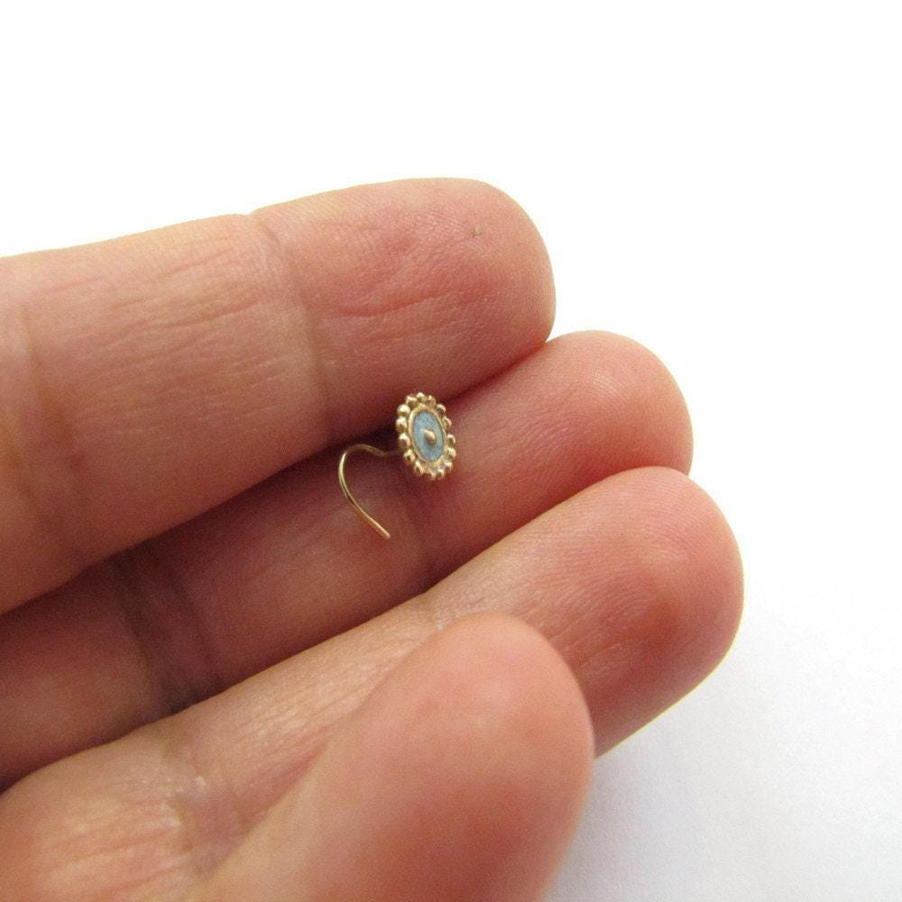 A hand holding a small gold-colored nose stud.
