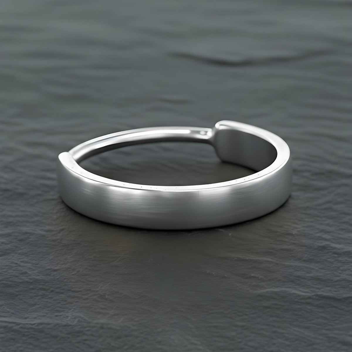 A silver ring with a curved band sits on a dark surface, creating a striking contrast.