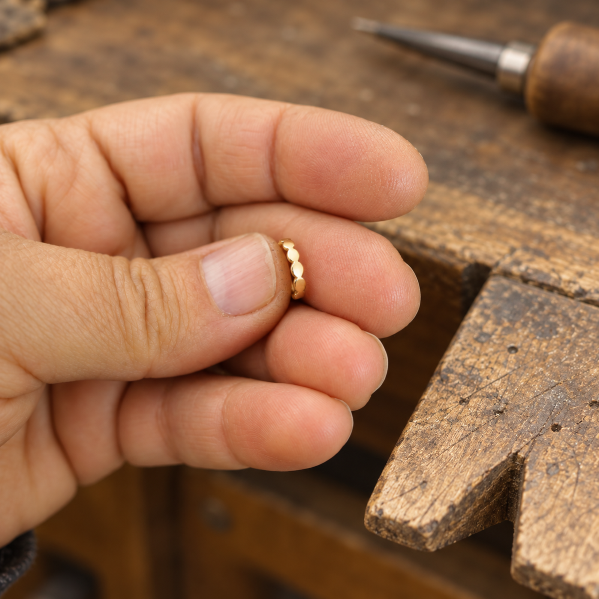 A person's hand holding a small gold-colored ring on a wooden surface.