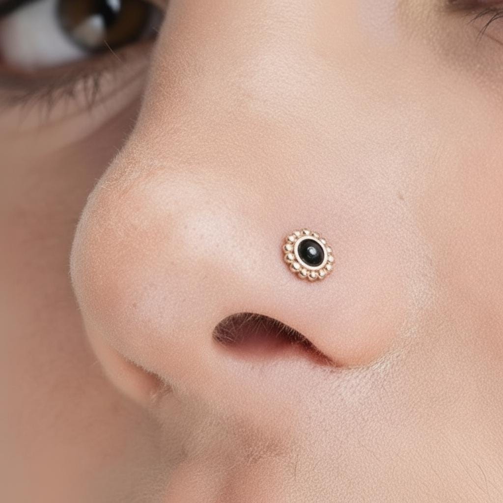 A close-up of a person's nose with a small, ornate nose ring featuring a black stone or gemstone in the center.