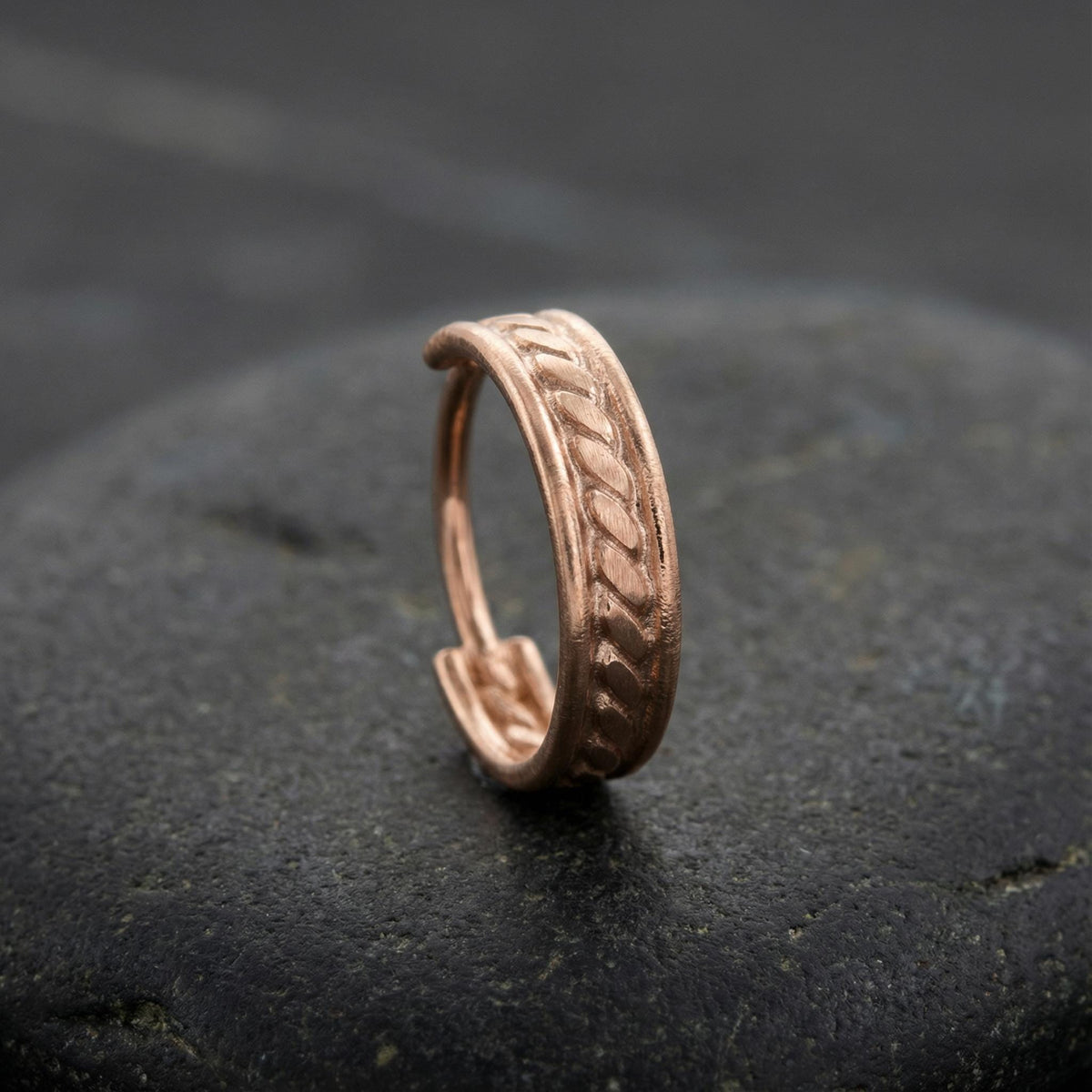 A copper-colored ring with a braided pattern sits on a dark surface.