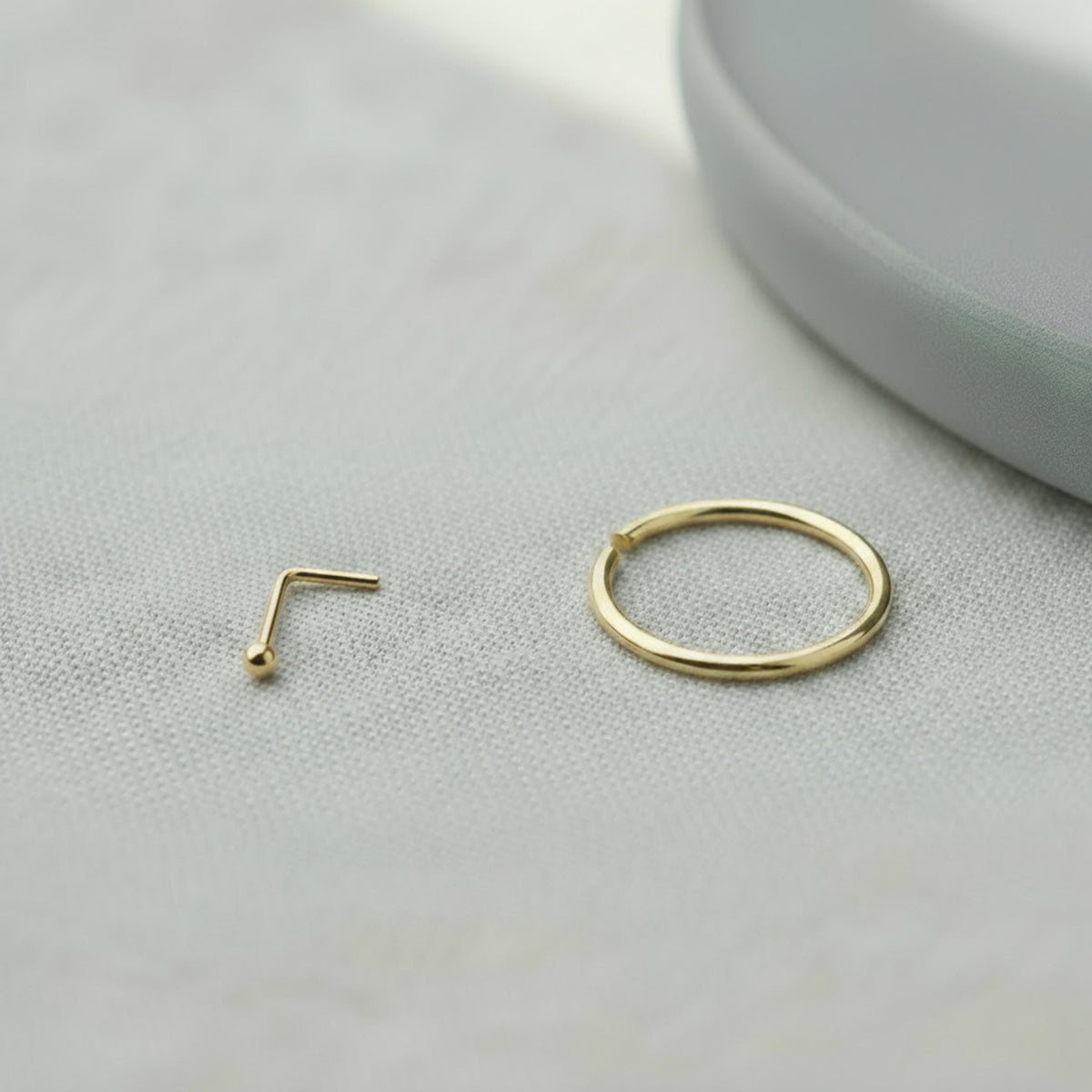 A gold-colored nose ring and a gold-colored ring are placed on a white surface.