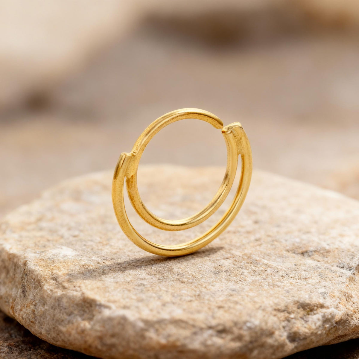 A gold-colored ring with a circular design sits on a rock.