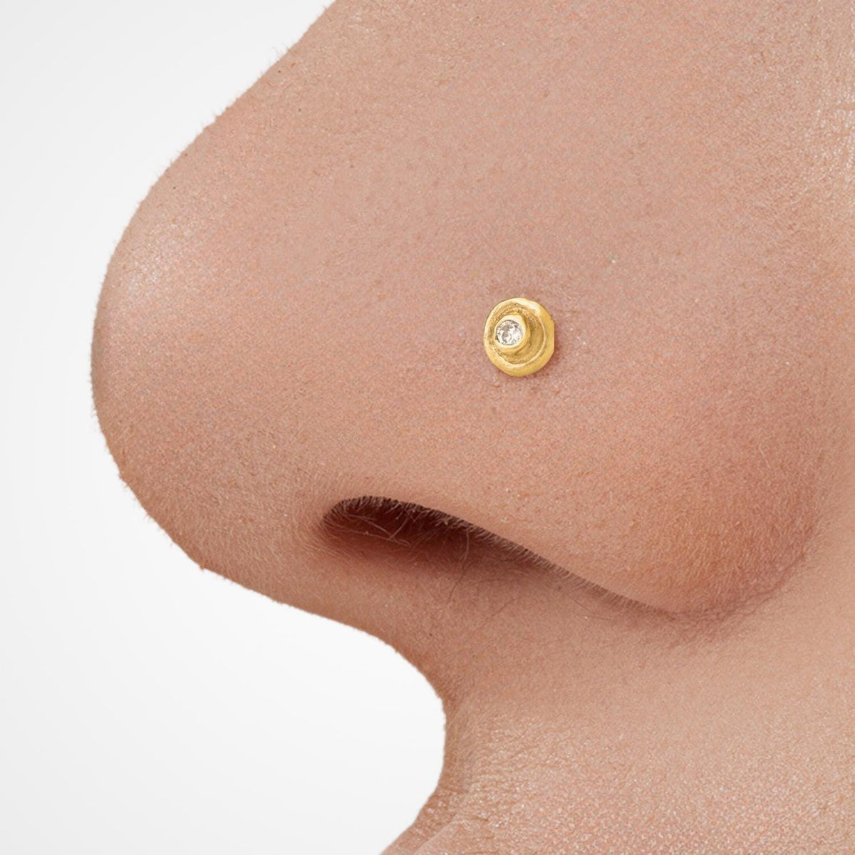 Diamond Nose Stud: A close-up of a person's nose with a small gold-colored nose ring with a diamond in the center.