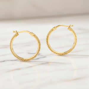 Boho 14k Gold Hoop Earrings: A pair of gold hoop earrings with small, round stones or beads around the outer edge, resting on a marble surface.