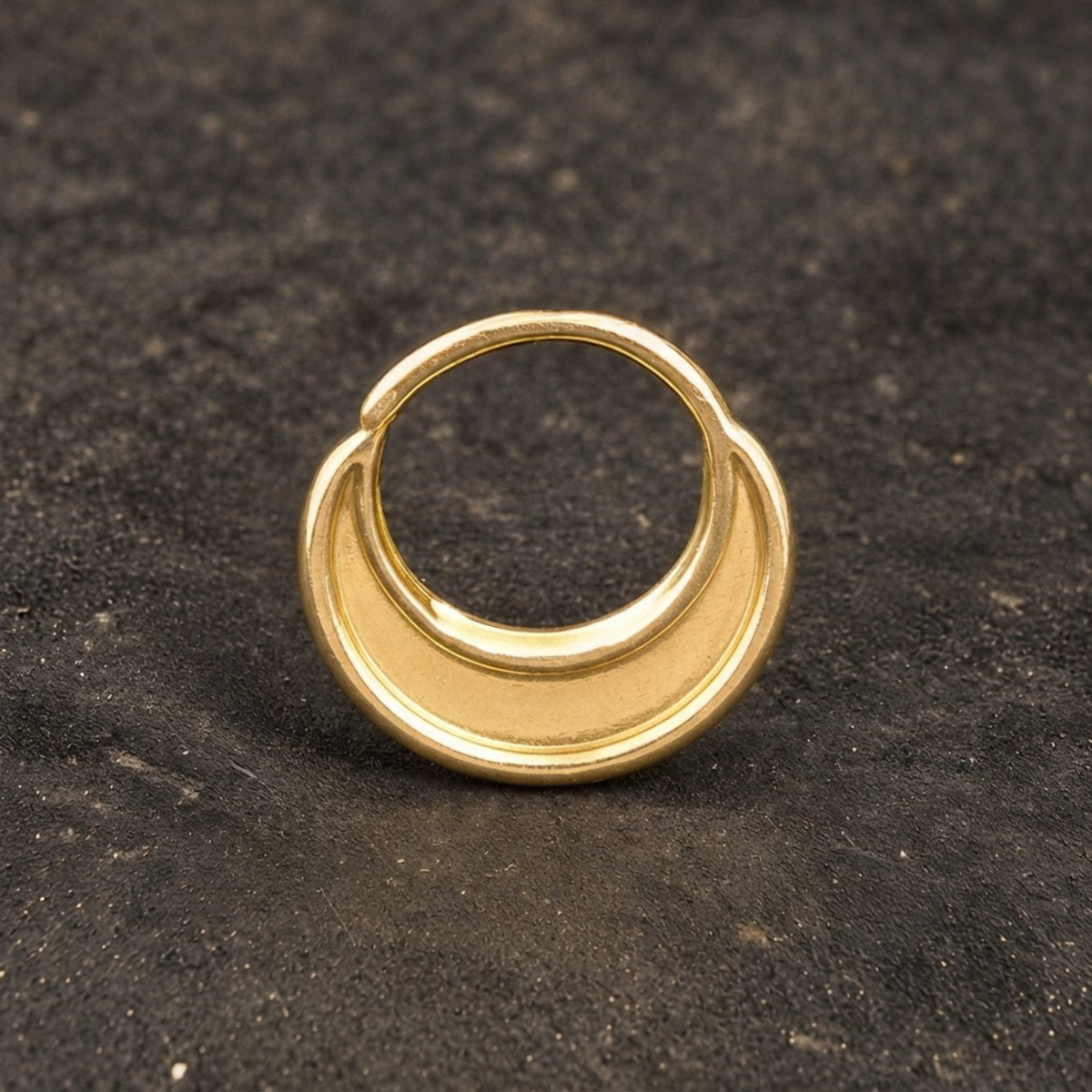 A gold ring with a crescent-shaped design is shown against a dark background.
