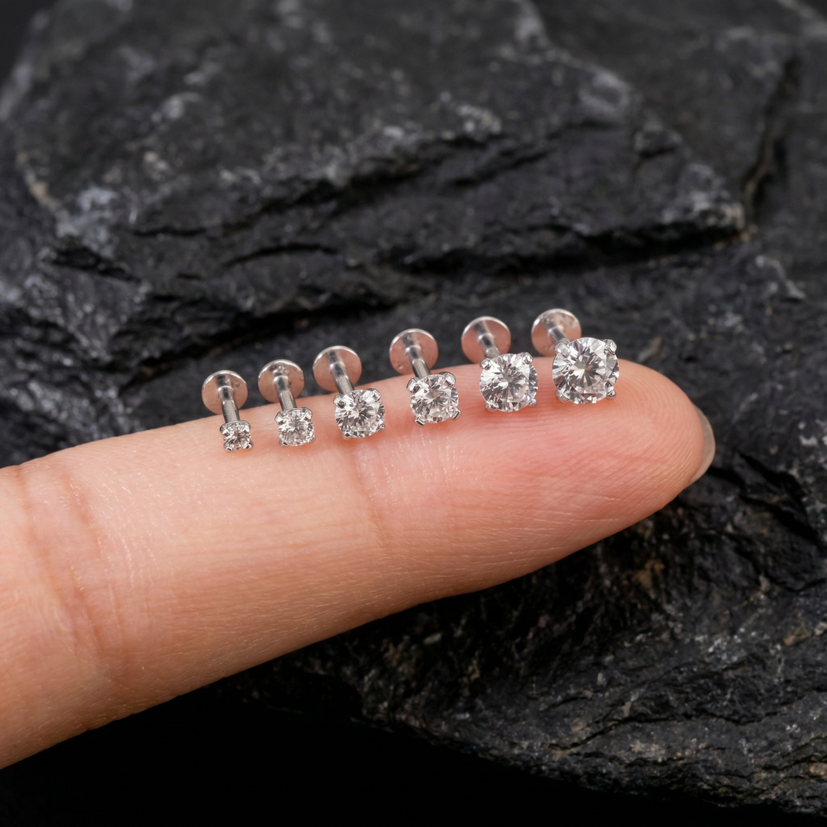 A close-up image of a person's finger wearing a row of six silver earrings with clear gemstones.