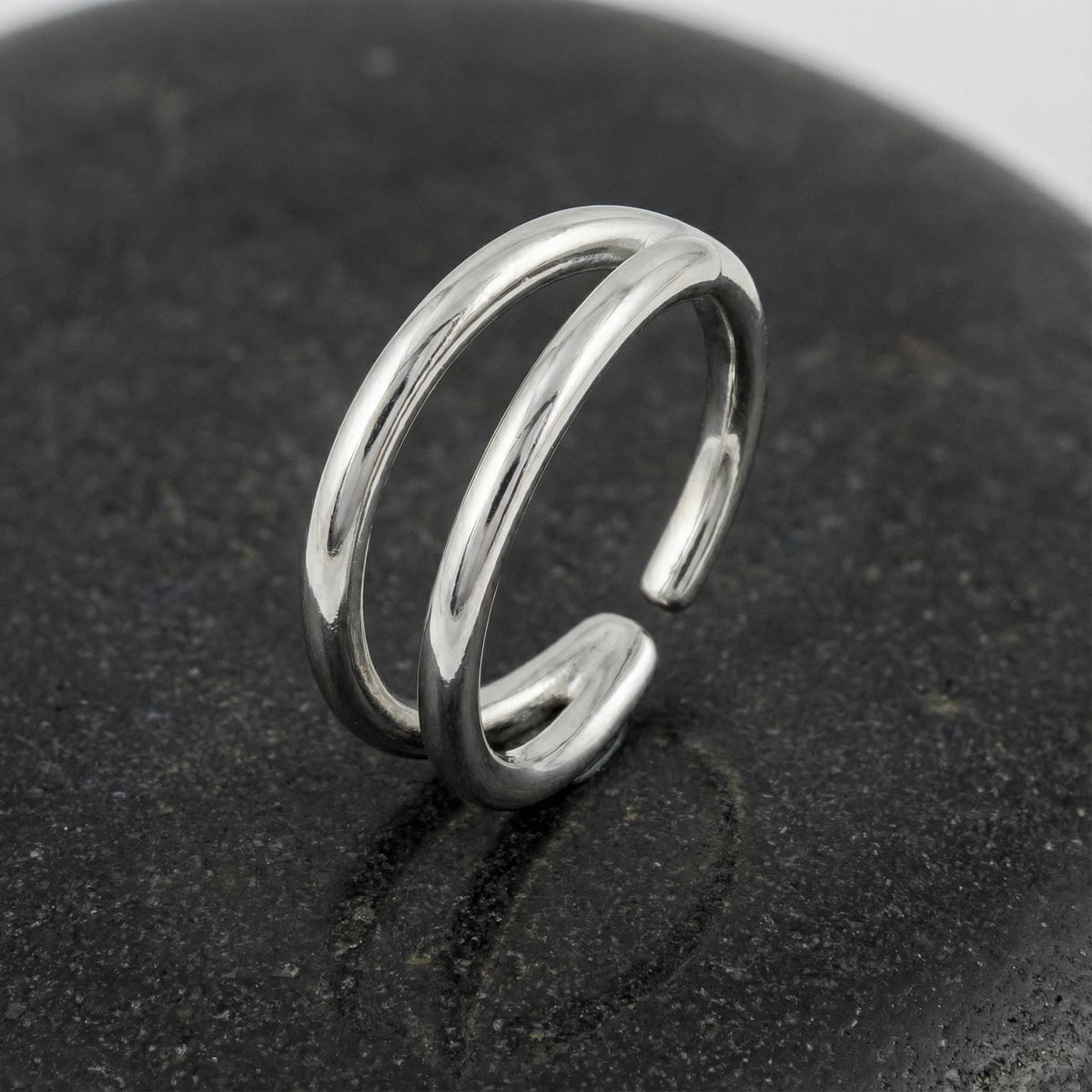 A silver ring with a unique, double-ended design is resting on a black surface.