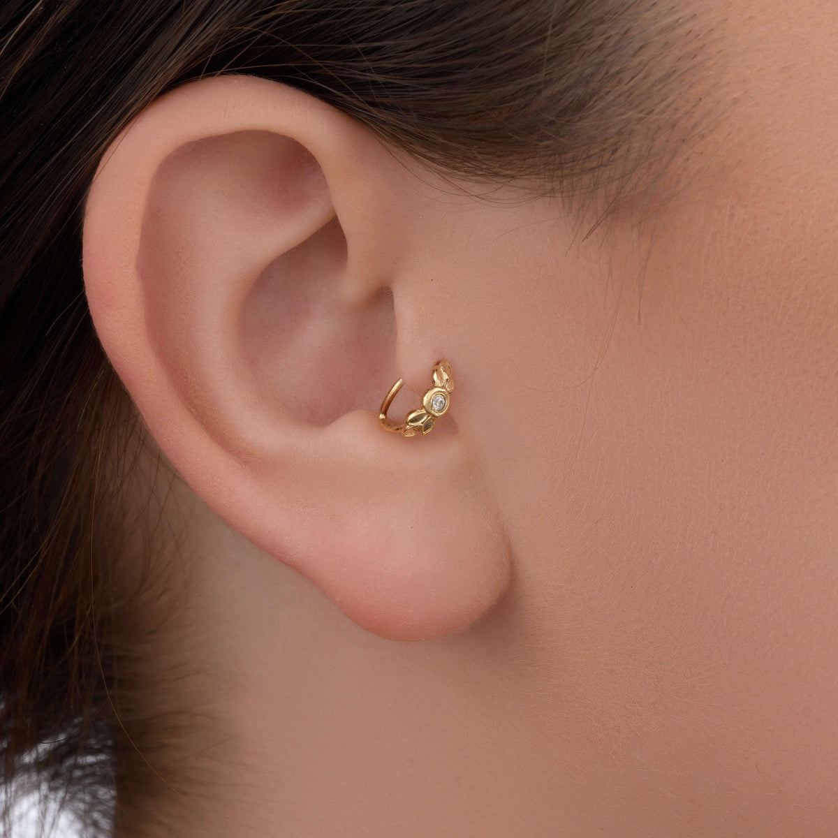 A close-up view of a person's ear with a gold earring featuring a floral design.