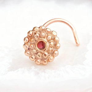 Indian Tribal Nose Stud: A gold-colored nose ring with a red gemstone is displayed on a white and gold decorative plate.