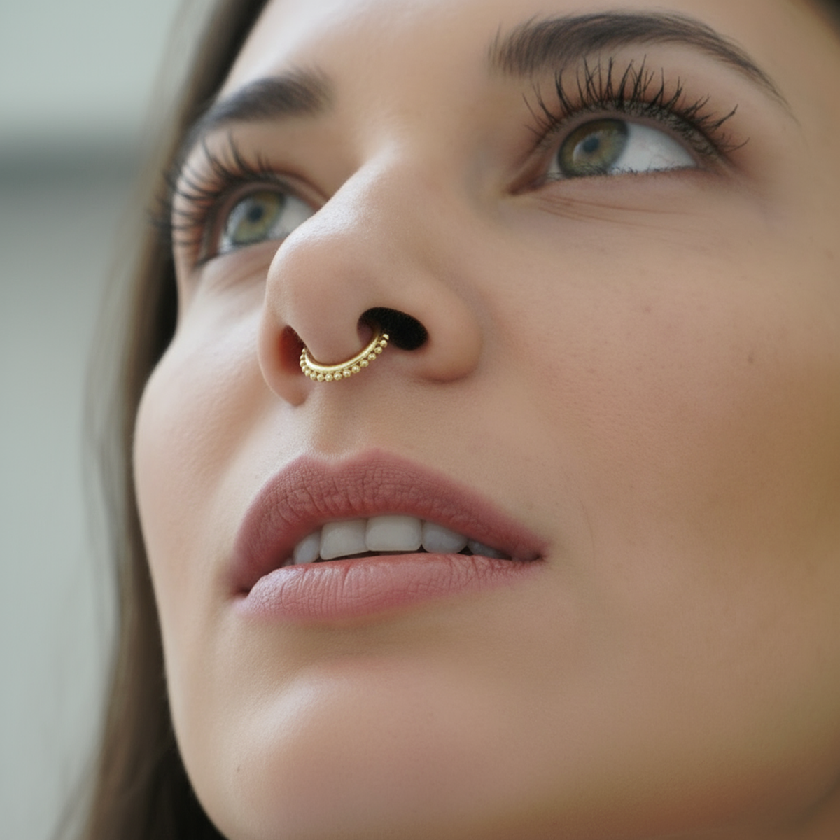 A close-up of a woman's face, focusing on her nose and lips, with a gold nose ring visible.