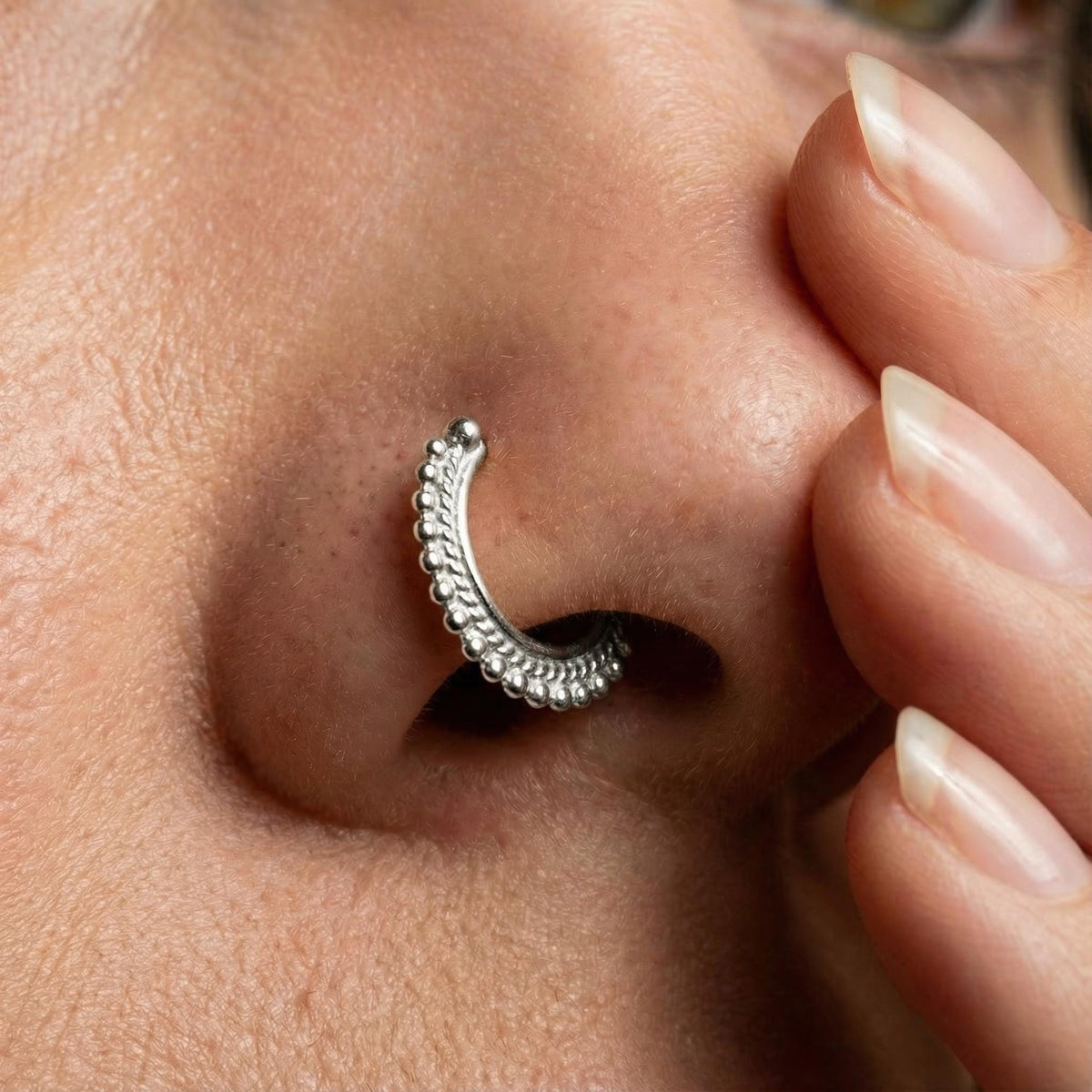 Indian Nose Ring Hoop: A close-up of a person's nose with a decorative metal ring or piercing in it.