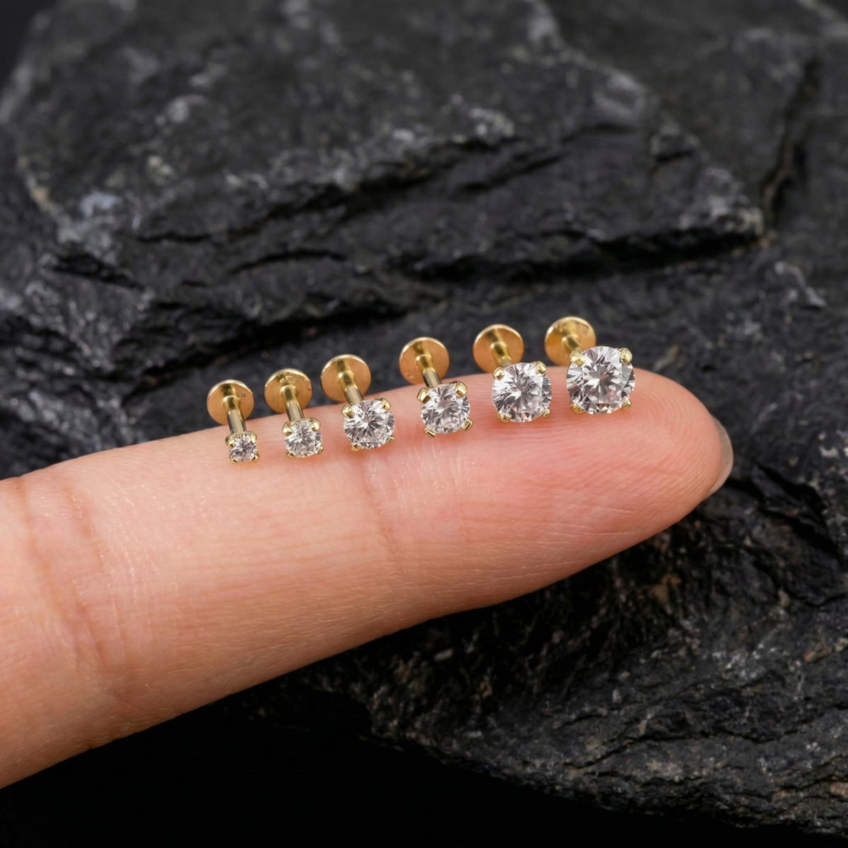 A close-up image of a person's finger wearing a row of gold-colored diamond stud earrings.