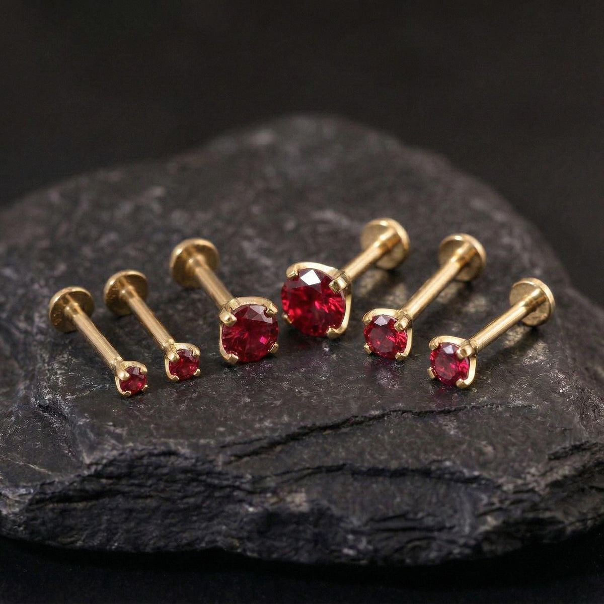 A collection of gold-colored earrings with red gemstones, arranged on a dark surface.