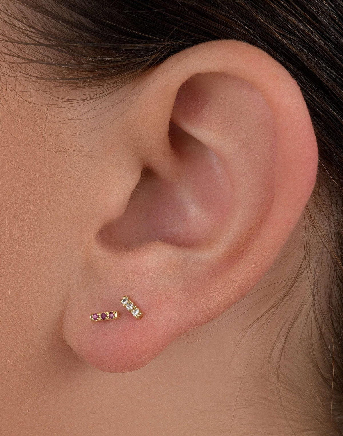 A close-up view of a person's ear adorned with two small gold earrings, each featuring a small gemstone.