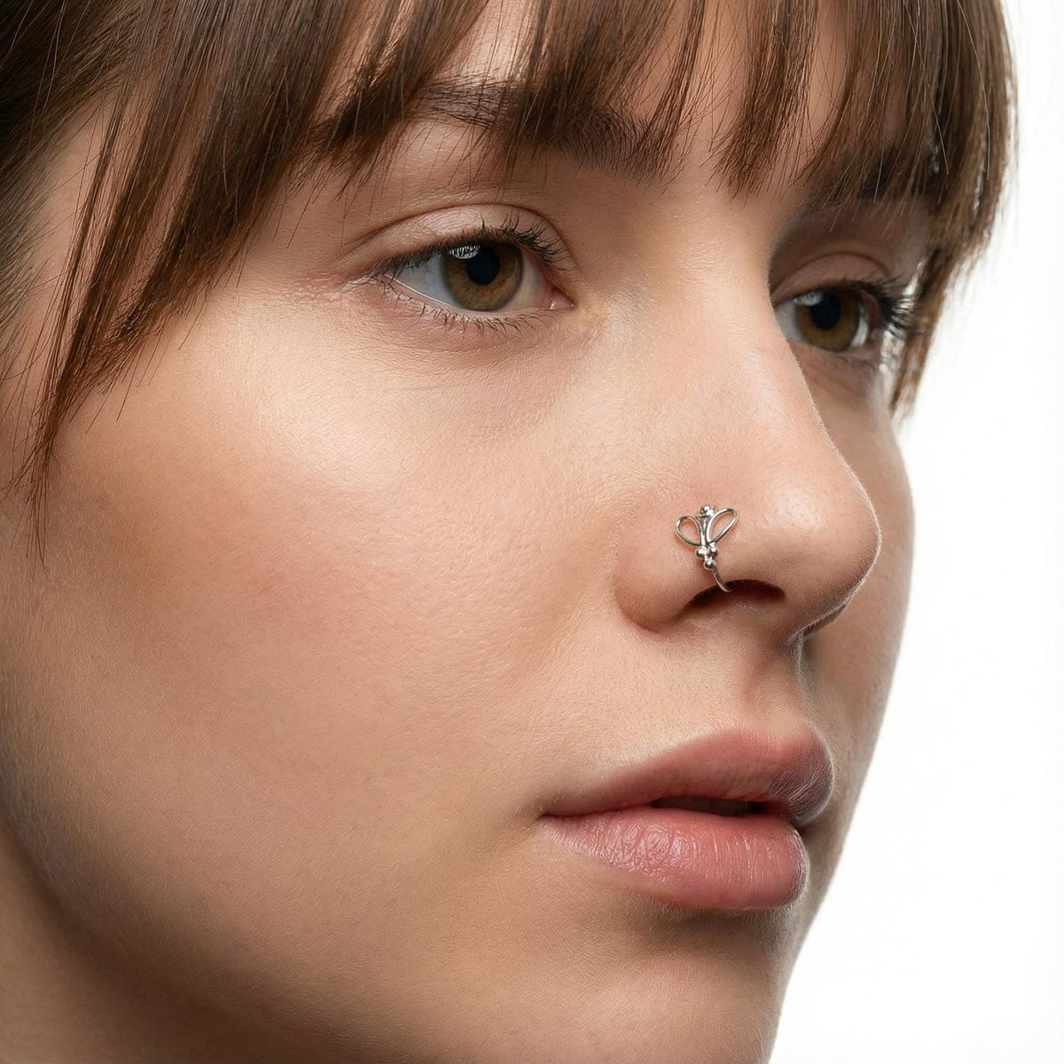 A close-up portrait of a woman with brown hair and a nose ring, looking directly at the camera with a neutral expression.