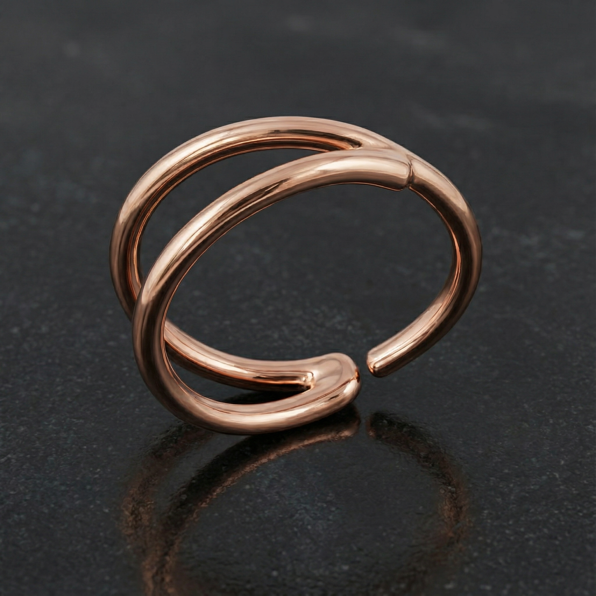 A shiny, metallic ring with a unique, twisted design sits on a dark surface.