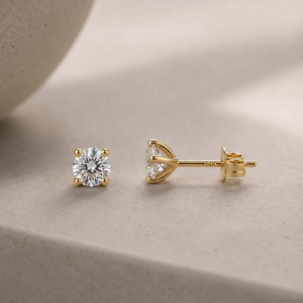 A pair of gold earrings with a large diamond set in the center, resting on a light-colored surface.