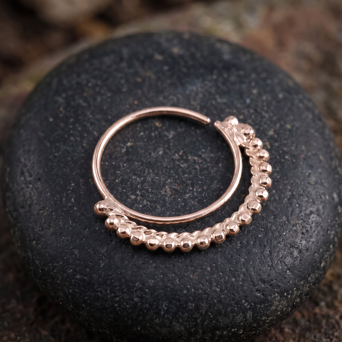 A gold-colored metal ring with a decorative clasp is resting on a dark, textured surface.